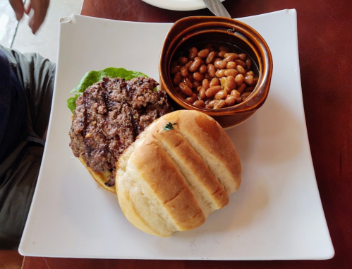 A plate with a hamburger topped with lettuce and a side of baked beans in a small bowl.