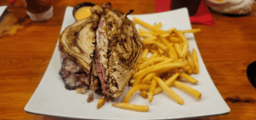 A large sandwich with layers of meat and cheese, served with a side of golden French fries on a white plate.