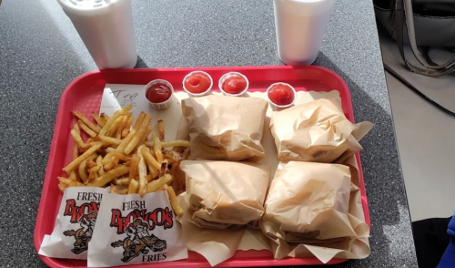 A red tray with four wrapped burgers, fries, ketchup cups, and two drinks.
