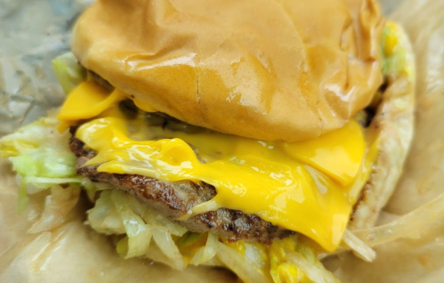 Close-up of a cheeseburger with melted cheese, lettuce, and a soft bun, resting on a piece of parchment paper.