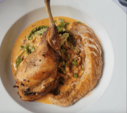 A plate featuring a roasted chicken leg, creamy sauce, and a side of tender vegetables.