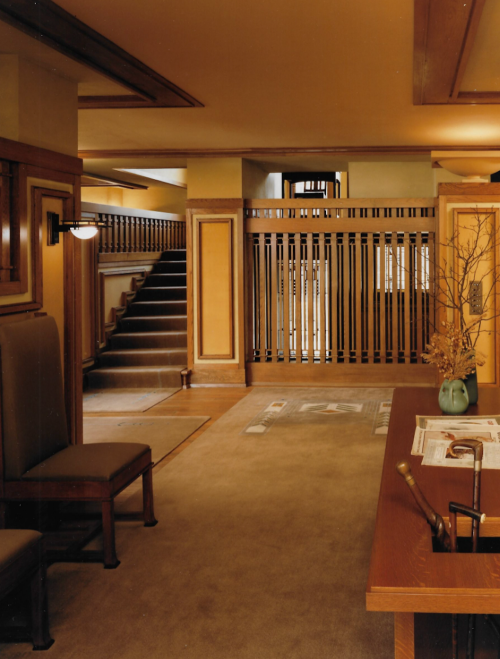 Interior of a warm-toned room featuring a staircase, wooden railings, and a desk with a vase.