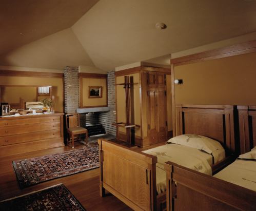 Cozy bedroom featuring wooden furniture, a fireplace, and a patterned rug, with warm, earthy tones.