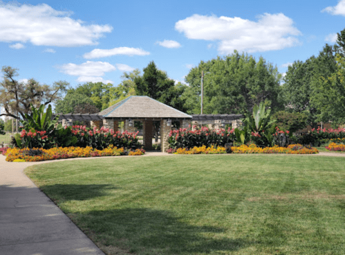 A landscaped garden with colorful flowers surrounds a stone building under a blue sky with fluffy clouds.
