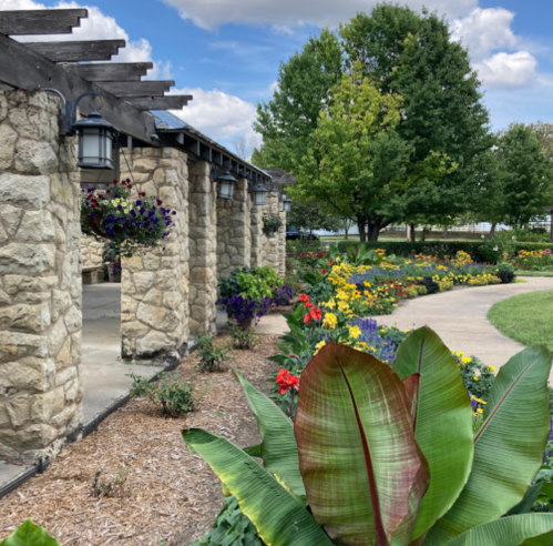 A landscaped garden with stone columns, colorful flowers, and lush greenery under a clear blue sky.