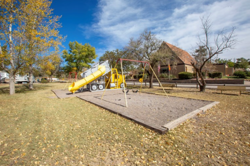 A playground featuring a yellow slide, swings, and trees with autumn leaves under a blue sky.