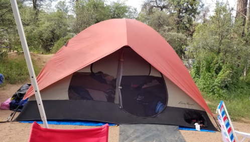 A large orange tent set up in a wooded area, with a view of the entrance and surrounding greenery.