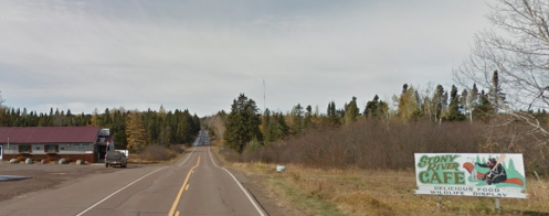 A rural road leads to Stony River Café, surrounded by trees and featuring a wildlife display sign.