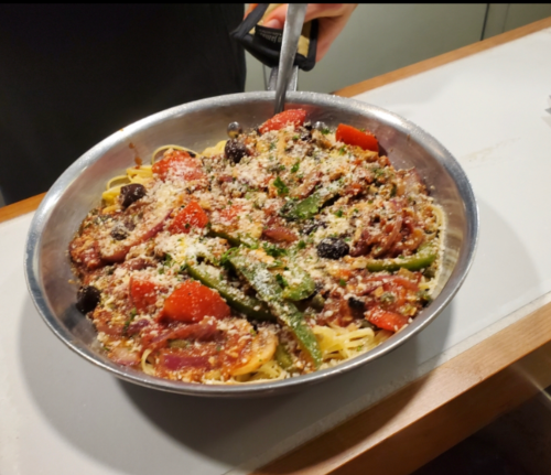 A large bowl of pasta topped with vegetables, herbs, and cheese, being served with a fork.