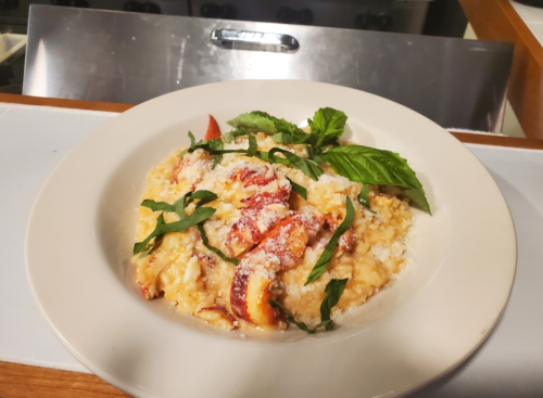 A creamy risotto topped with lobster, fresh basil, and grated cheese, served in a white bowl.