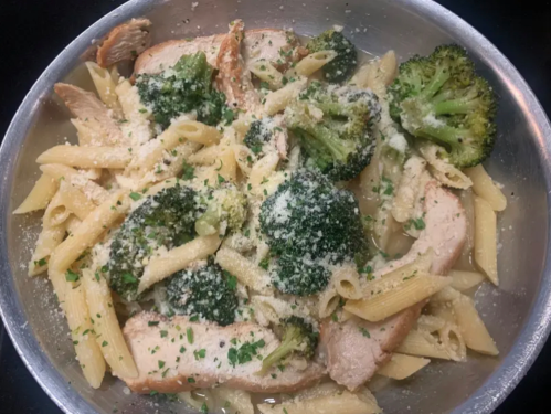 A bowl of pasta with chicken, broccoli, and grated cheese, garnished with herbs.
