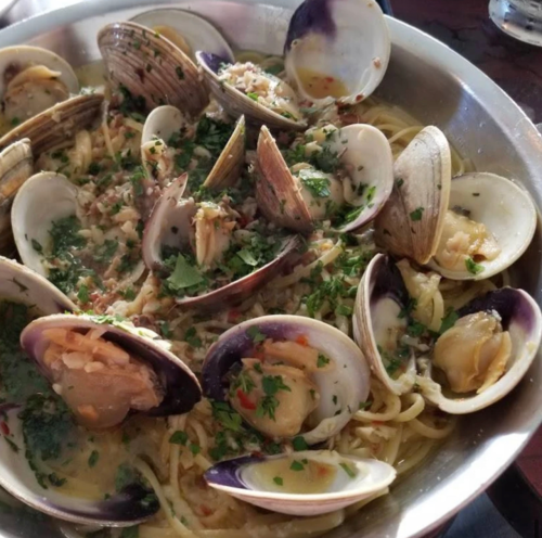 A close-up of spaghetti with clams, garnished with herbs in a large metal bowl.