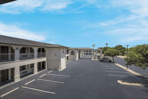 A view of a motel with a parking lot, blue sky, and trees in the background.