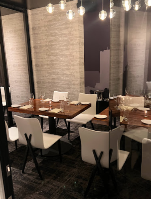 A modern dining room with a wooden table set for dinner, surrounded by white chairs and stylish pendant lights.