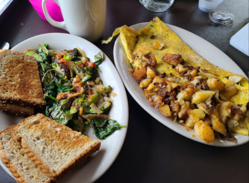 A plate with an omelet, seasoned potatoes, and a side of toast and salad on a table.