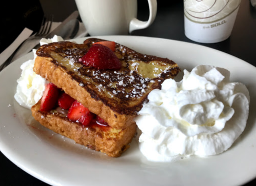 A plate of French toast layered with strawberries and whipped cream, dusted with powdered sugar.