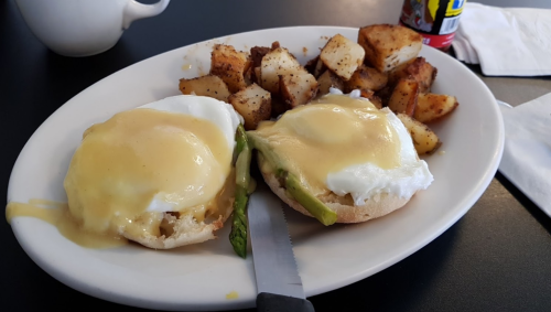 A plate of eggs Benedict with poached eggs, hollandaise sauce, and seasoned potatoes on the side.