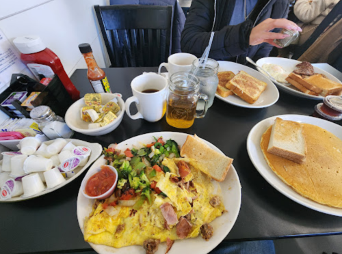 A table set with a hearty breakfast: an omelette, toast, pancakes, coffee, and condiments.