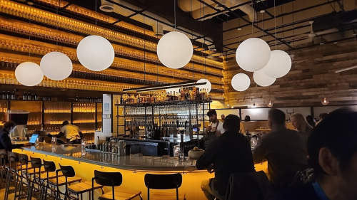 A modern bar with glowing round lights, wooden accents, and patrons seated at the counter.