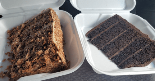 Two slices of cake in takeout containers: one is a layered carrot cake, the other is a rich chocolate cake.