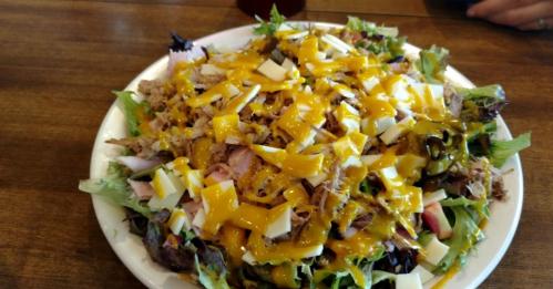 A large salad topped with shredded chicken, ham, cheese, and drizzled with yellow dressing on a white plate.