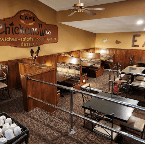 Cozy café interior with wooden booths, tables, and a sign reading "Chickanellas" on the wall.