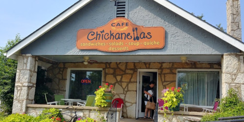 A cozy café with a stone exterior and a sign reading "Chickanellas," featuring outdoor seating and an "Open" sign.