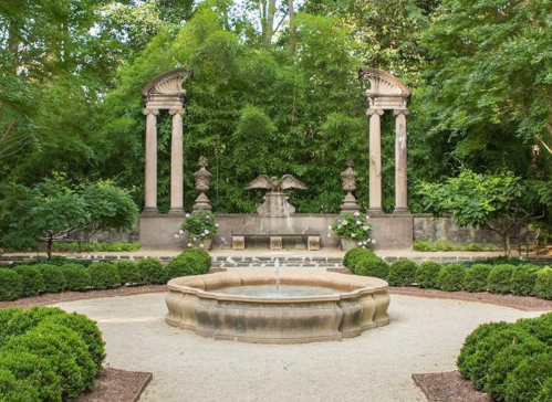 A serene garden with a central fountain, flanked by classical columns and lush greenery.