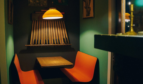 Cozy corner booth with orange seating, a wooden table, and a warm pendant light in a stylish interior.