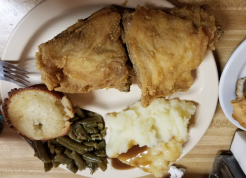A plate of fried chicken, mashed potatoes with gravy, green beans, and a slice of cornbread.