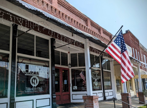 A storefront with a sign reading "Nick's Place" and an American flag hanging outside.