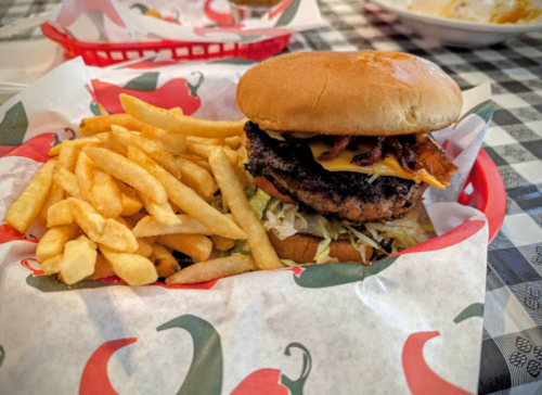 A burger with bacon and cheese on a bun, served with a side of golden fries in a red basket.