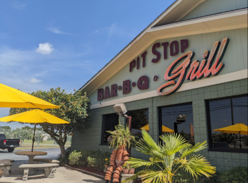 Exterior of Pit Stop Bar-B-Q & Grill with yellow umbrellas, greenery, and a clear blue sky.