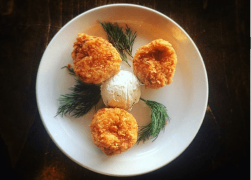 Three golden fried patties arranged around a scoop of ice cream, garnished with fresh dill on a white plate.