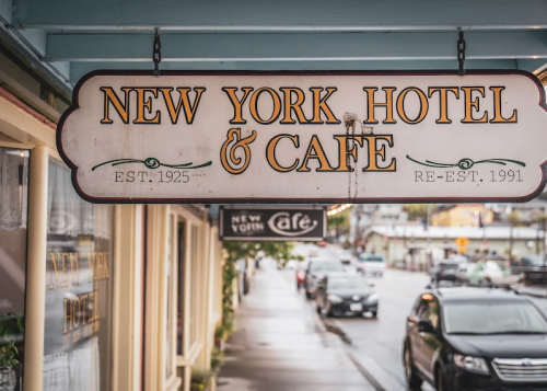 Sign for "New York Hotel & Café," established in 1925 and re-established in 1991, with a rainy street view.