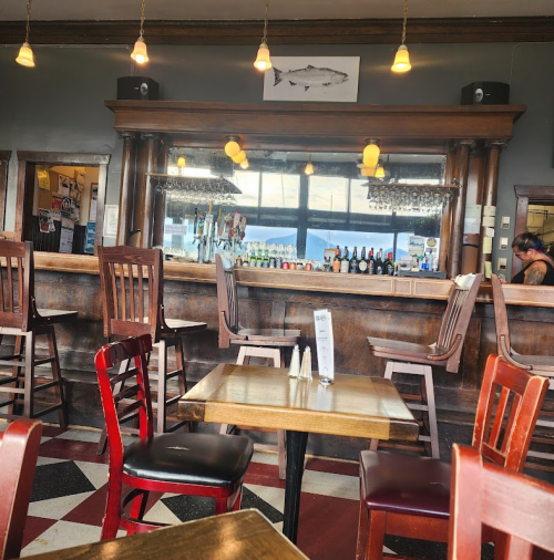 Interior of a rustic bar with wooden chairs, a mirrored back bar, and a view of a lake through large windows.