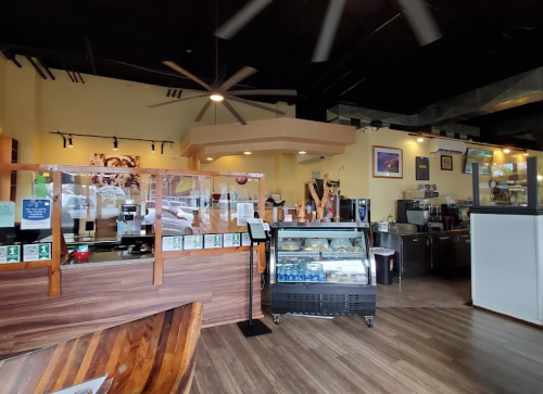 Interior of a cozy café featuring a counter, display case, and seating area with wooden accents and large ceiling fans.