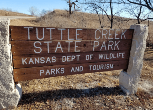 Wooden sign for Tuttle Creek State Park, Kansas, displaying park name and department information.