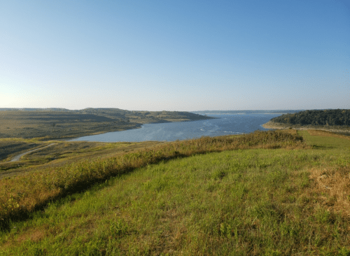 A serene landscape featuring a river winding through green hills under a clear blue sky.