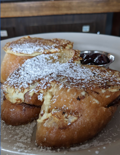 A plate of French toast dusted with powdered sugar, served with a small cup of berry jam.