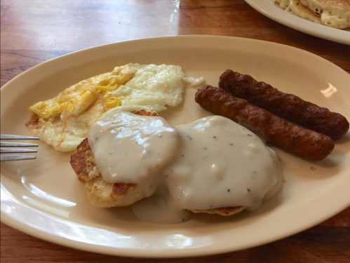 A plate with two sausage links, a fried egg, and biscuits topped with creamy gravy.