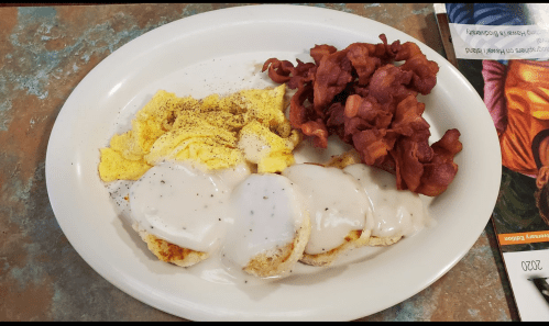 A plate of scrambled eggs, biscuits with gravy, and crispy bacon.
