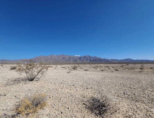A vast desert landscape with sparse vegetation and distant mountains under a clear blue sky.