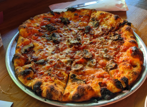 A freshly baked pizza with a golden crust, topped with melted cheese and various toppings, sliced into wedges.