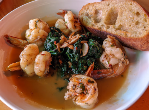 A bowl of shrimp with sautéed greens and sliced almonds, served with a piece of crusty bread on the side.