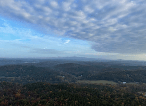 A panoramic view of rolling hills and valleys under a cloudy sky, showcasing autumn foliage in the landscape.