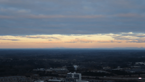 A panoramic view of a landscape at dusk, with clouds and a colorful horizon over distant mountains.
