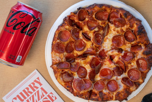A pepperoni pizza on a white plate next to a can of cola and a menu titled "Curry Pizza House."