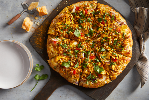 A freshly baked pizza topped with vegetables, herbs, and spices, sliced and served on a wooden board.