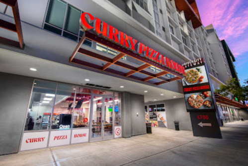 Exterior of Curry Pizza House with a modern design, featuring large windows and a vibrant sign at dusk.